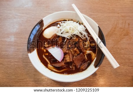 A bowl of Kishimen flat noodle with chopstick - Local Nagoya Kihimen noodle with Miso soup, Tofu, pork belly top with sliced Kamaboko fish cake, egg, leek. Royalty-Free Stock Photo #1209225109