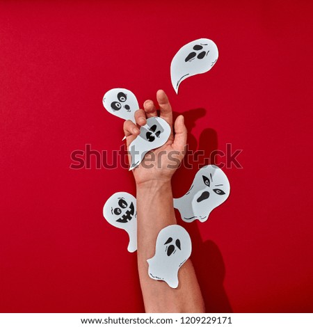 Paper handcraft work various ghosts decorate the hand of a man on a red background with space for text. Halloween creative composition. Flat lay