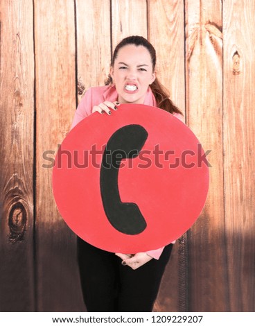 Portrait of an angry young woman holding a missed call sign against a wooden background