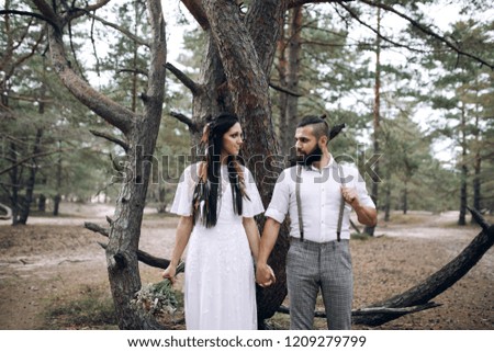 Modern bride and groom stand at wood, behind dry tree