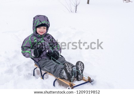 Happy kid walking outdoors in winter city drags his sled. Happy child smiling and having fun