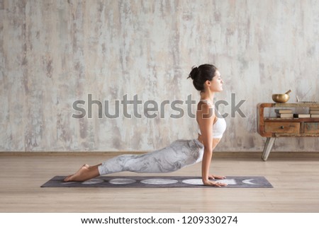Young indian girl doing yoga fitness exercise indoor. Wellness concept. Calmness and relax. Yogi Instructor doing Urdhva mukha shvanasana exercise, upward facing dog pose, working out, home interior Royalty-Free Stock Photo #1209330274