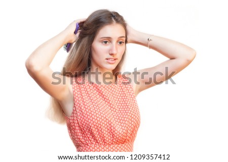 A girl with blond hair on a white background hairstyles herself and makes herself a hairdo, in her hands she holds her comb. Copy space. Isolated