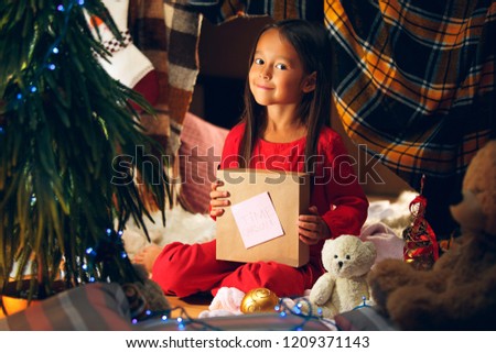 Merry Christmas and Happy Holidays. Cute little child girl writes the letter to Santa Claus near Christmas tree at home indoor. The holiday, childhood, winter, celebration concept