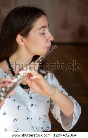 A gorgeous young woman sitting and playing the flute Close-up