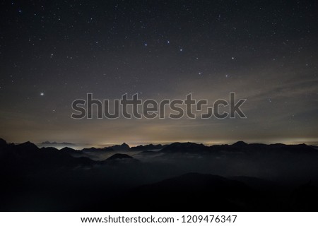 Clouds rolling over the mountains of the alps at night time with a starry sky and the constellation Big Dipper Royalty-Free Stock Photo #1209476347