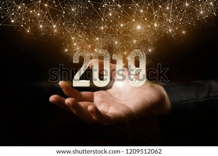 The 2019 number of the yea is flying above the hand emitting bright , holiday lights. The concept is New Year.