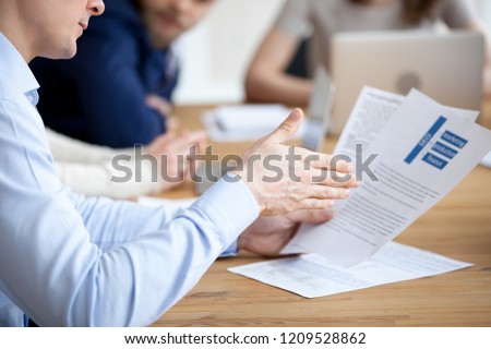 Close up of male employee read paper handout material during office meeting, man analyzing paperwork report at briefing, explaining content to colleague, worker sit at desk looking through document Royalty-Free Stock Photo #1209528862
