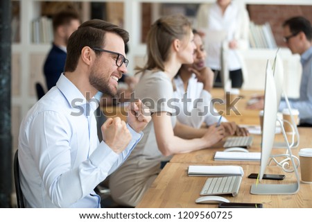 Excited millennial male employee work in shared workplace winning online lottery, happy worker gesture yes getting job promotion achieving goal, satisfied man feel euphoric reading great news online Royalty-Free Stock Photo #1209560725