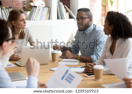 African American employee talk at briefing expressing point of view, multiracial millennial workers brainstorm in boardroom discussing project report, diverse colleagues negotiate at business meeting Royalty-Free Stock Photo #1209569923