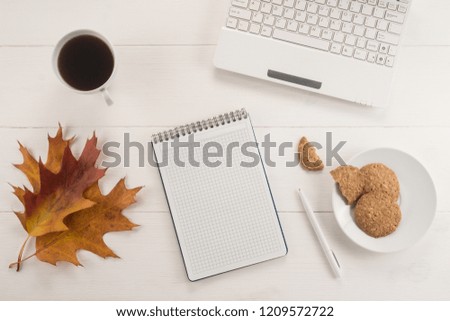 Office table with a cup of coffee, cookies and autumn leaves on wooden background