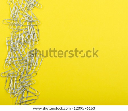 Heap of note paper clips on yellow background top view. Pile of steel clips or paperclips with copyspace