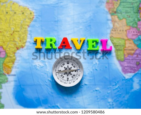 metal compass and word - travel made from colorful letters lie on world blue map