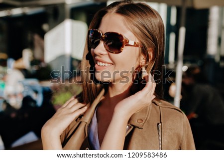 Close-up portrait of cheerful white woman in glasses touching her hair on blur background. Pretty lady with wonderful smile spend time outside and shows good mood
