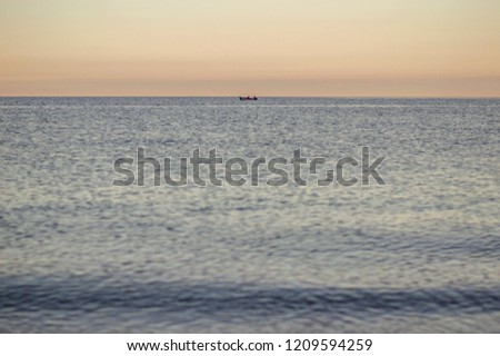 Calm empty sea in the sunset or sunrise with a single small silhouette of a fishing boat in the distance