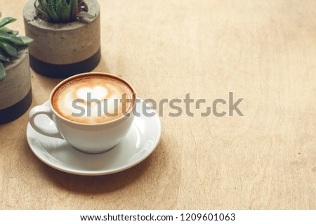 Cup of cappuccino with latte art on wooden background with plant. Hot coffee with flower on table. Top view, flat lay copy space for text. Beautiful foam, top view, copy space.