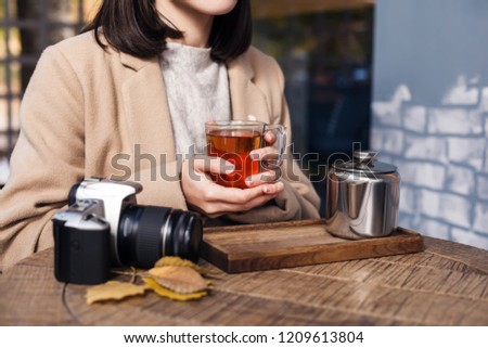A girl with a camera is drinking tea at a table in a cafe. Closeup. Autumn concept Royalty-Free Stock Photo #1209613804