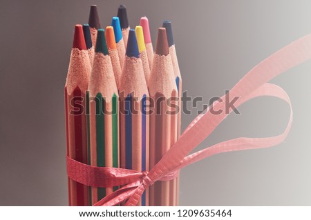 Group of multicolored pencils decorated with red gift ribbon.