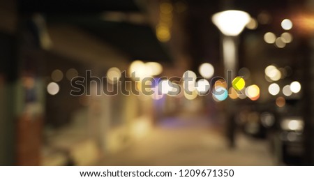 View down urban sidewalk of store fronts and bokeh lights in evening