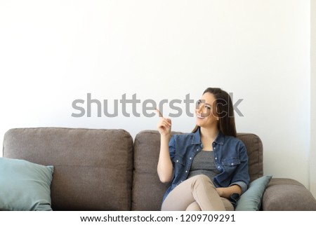 Woman sitting on a couch pointing at a white wall isolated