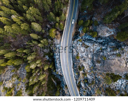 Aerial drone photo of Cars driving along road in opposite direction through pine tree forest and rock at emerald lake, lake tahoe, california USA