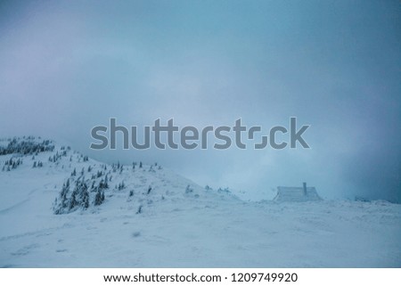 A small house in the mountains. A snow-covered hut against the background of a winter forest and a beautiful sky with clouds. Mountain landscape.