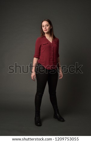 
full length portrait of brunette girl wearing  red shirt and leather pants. standing pose , on grey studio background.
