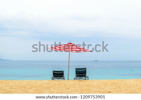 Idyllic tropical Caribbean island summer beach vacation setting. Two empty lounge/sun chairs under large red & white striped patio umbrella on beautiful white sand by the ocean in Montego Bay Jamaica