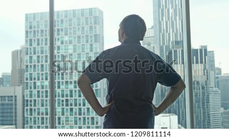Young successful rich man unveil curtains and admire the city center with skyscrapers view