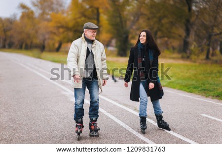 Active old people. The old man goes on rollers with his daughter in the autumn park. Happy pension. Active old people.The old man goes on rollers with his daughter in the autumn park. Happy pension.