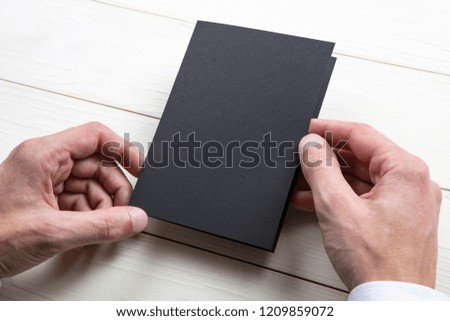 Mens hands holding empty black booklet on gray background. View from above