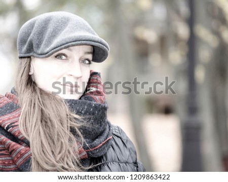 Portrait of a young girl. A cheerful look, a smile on his lips. Warm wool cap and voluminous scarf. Somewhere in nature. Late autumn or winter. Blurred background. Copy space to add your text.
