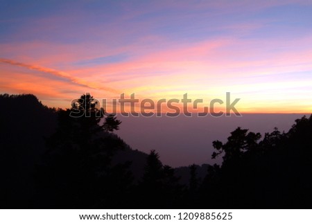Alpine mountain peak silhouette. Colored clouds, fog, sunshine, and rapid weather changes.