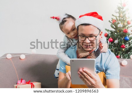Asian father and daughter using tablet together.Smiling face in room with Christmas tree decoration for holiday background.Family Christmas Party and celebration concept.