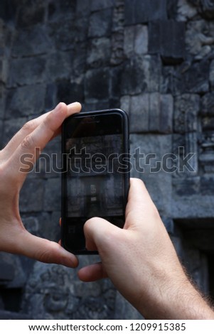 Close up of a man taking a picture with his mobile phone of old, ancient ruins