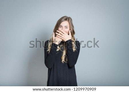 beautiful blond woman laughs and covers her mouth, isolated over gray background