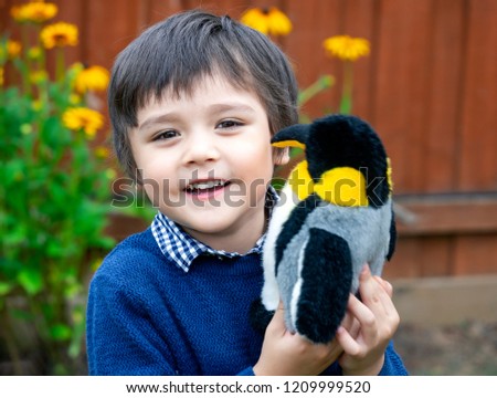 Portrait cute little boy with a happy face playing with penguin soft toy,Happy child having fun playing outdoors in the garden.