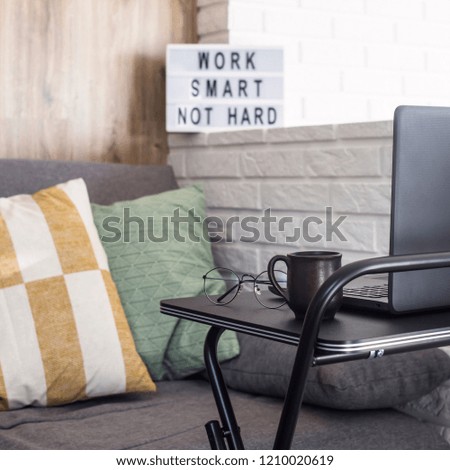 Home workplace of a freelancer at a black stylish table near the sofa and brick wall in a modern apartment. Work smart, no hard - written on a lamp