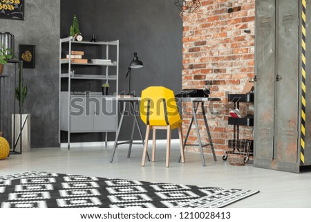 Yellow chair at desk in teenager's room interior with red brick wall and patterned carpet. Real photo