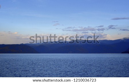 The western shore of Lake Teletsky is set at sunset, the setting sun tingles white cumulus clouds orange. The picture was taken on an autumn evening, with natural light.
