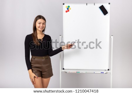 Portrait of a smiling red haired businesswoman standing with a marker near a whiteboard and drawing a graph. Toned image.
