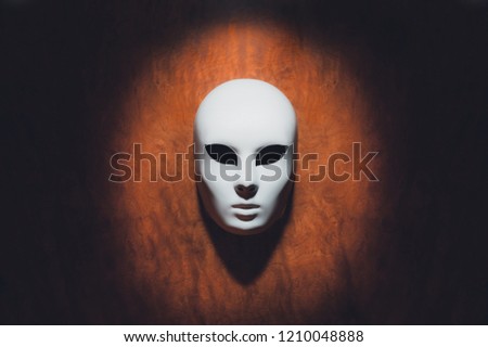 White mask in dramatic light on wooden background. Theatre concept. Copy space.