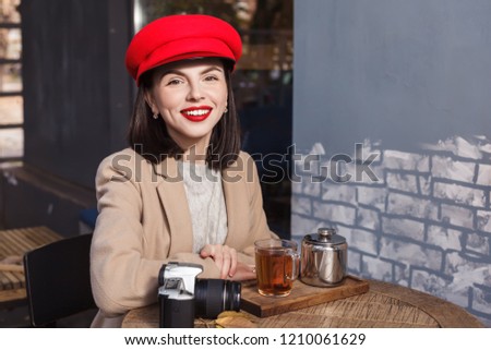 Young beautiful girl in red hat is drinking tea in a cafe
