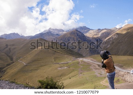 Young curly traveler taking photo with camera in Kazbegi. Beautiful view of Kazbegi in autumn