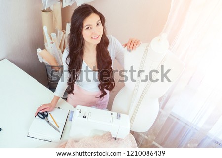 beautiful woman seamstress with long hair hugging maniken. tailor creates a collection of clothes on the background of a sewing machine and a manicure. The concept of sewing and fashion design
