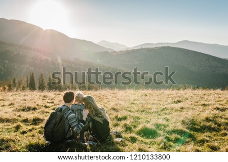 Happy Hipster family: mom, dad, daughter with backpack enjoying sunset on peak of foggy mountain. Tourists traveler on background view mockup. Hikers looking sunlight in trip in country Europe.
