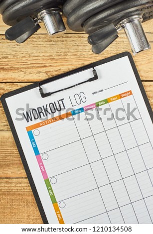 Healthy lifestyle concept. Mock up on workout and fitness dieting diary. Workout log sheet and dumbbells on a wooden background. Royalty-Free Stock Photo #1210134508