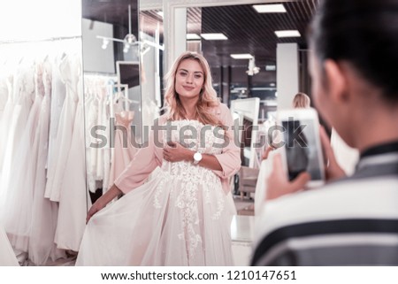 Great picture. Delighted joyful woman smiling while posing for a photo with a wedding dress