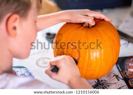 blond boy carving pumpkin jack-o-lantern with knife