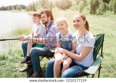 Nice family picture of four people catching fish together. Small girl is sitting on her mama's lap while small boy is doing the same thing but on his daddy's lap. Boys are holding fish-rod togther.